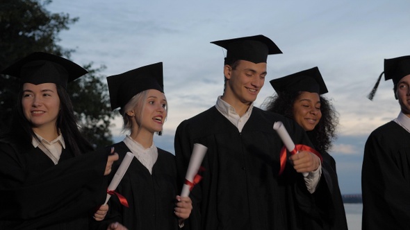 Happy smiled mixed races graduates walking with the diplomas