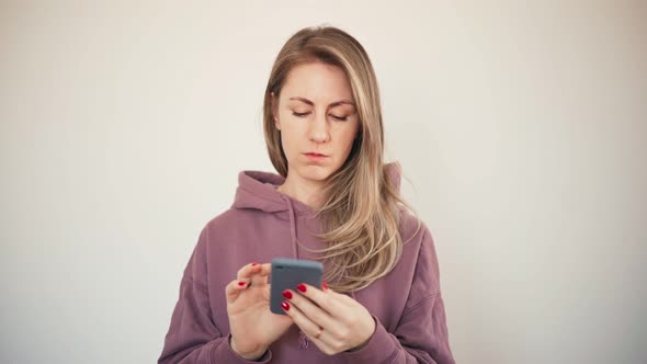 Beautiful Blond Woman in Hoodie Busy Typing a Message on a Smartphone
