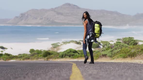 African american woman with backpack trying to hitch a lift while walking on road