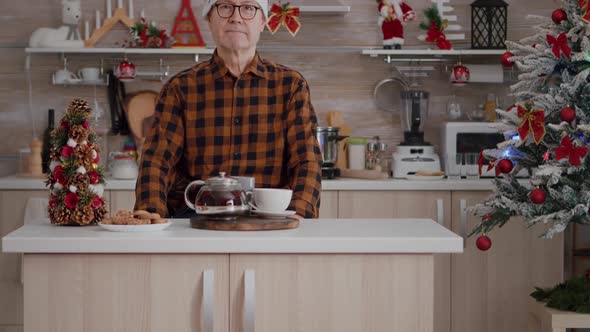 Portrait of Senior Man Wearing Santa Hat Smiling While Looking Into Camera During Christmas Morning