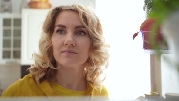 curly young woman opens refrigerator with healthy food and takes an apple Video 4k