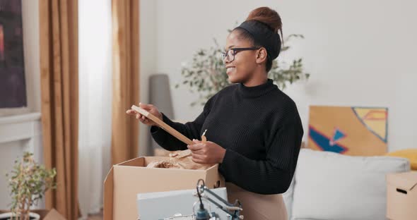 Finding Souvenirs During a Move a Woman in Glasses Unpacks a Cardboard Box in Which She Finds a