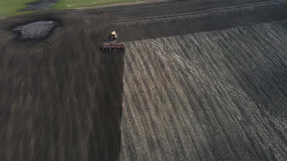 Aerial view of a modern yellow tractor plowing dry agricultural field , preparing land for sowing