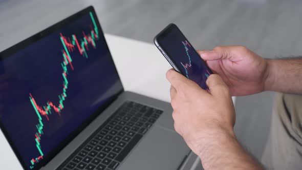 Millennial Young Adult Indian Male Stockbroker Using Phone and Laptop Indoors