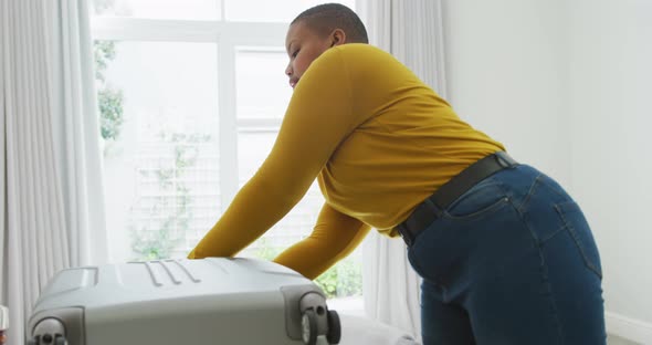 Happy african american plus size woman packing suitcase in bedroom