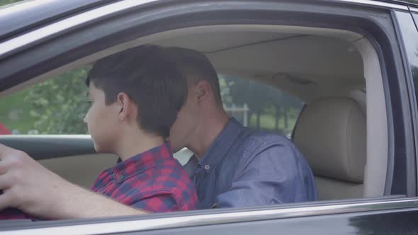 Young Father Teaching His Son To Drive the Car Close Up. The Boy Sitting on Father's Laps, Listening