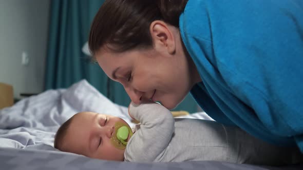 Young Mother Bends Kissing Hands of Baby Son Smiling Widely