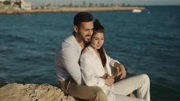 Smiling Ethnic Couple Talking on Rock Against Sea