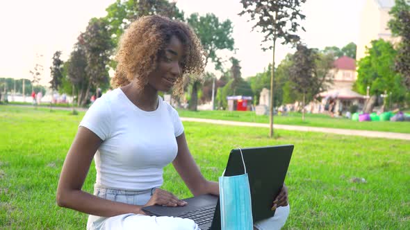 Young African American Woman Calling on Laptop Talks with Online Teacher Studying in the City Park