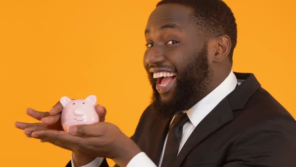 Smiling African-American Male Shaking Piggy Bank, Deposit Presents, Banking