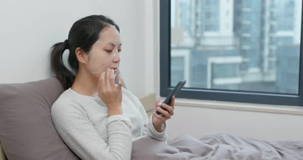 Woman use of cellphone and apply paper mask on face at home