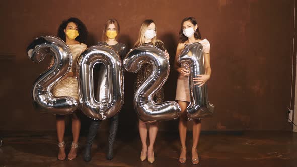 Four young international beautiful brunette women in trendy summer shiny dresses holding balloons