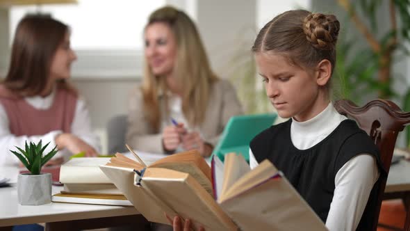 Genius Teenage Girl Reading Books Sitting in Classroom with Blurred Classmate and Teacher and