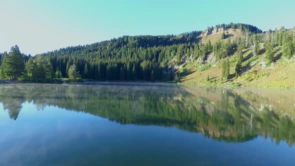 Steam slowly raises off a high mountain lake in the morning sun as the mountains are reflected in th