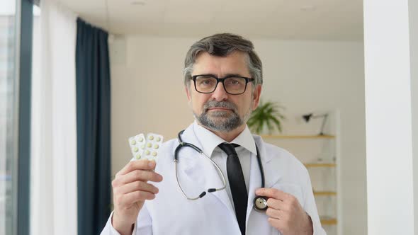 Senior Doctor Pharmacist Consultant Showing a Two Packs of Pills and Smiling in Camera