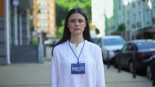 Serious Female Journalist With Microphone and Press Badge Looking at Camera, TV