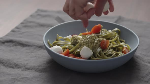 Slow Motion Man Hand Add Mozzarella Balls To Green Fettuccine with Pesto in Blue Bowl