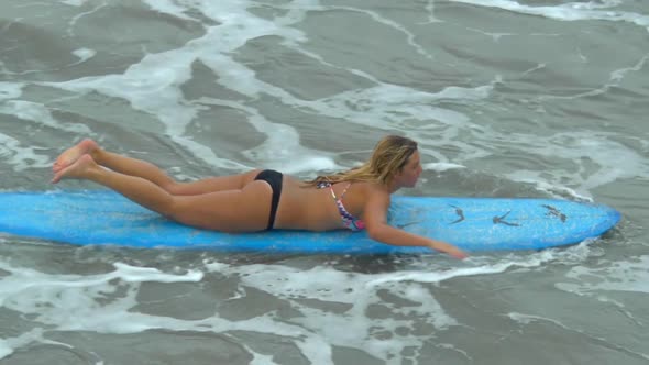 A young woman surfing in a bikini on a longboard surfboard.