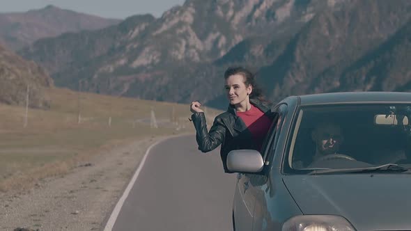 Smiling Brunette Sits with Raised Hand on Car Window