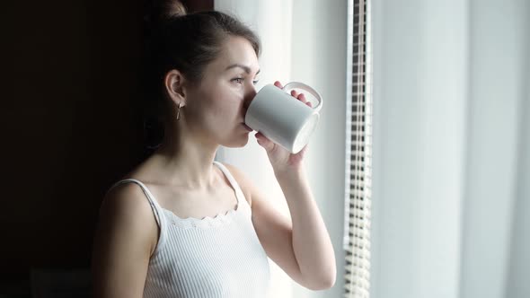 the girl goes to the window with a cup of coffee and pours red wine into it