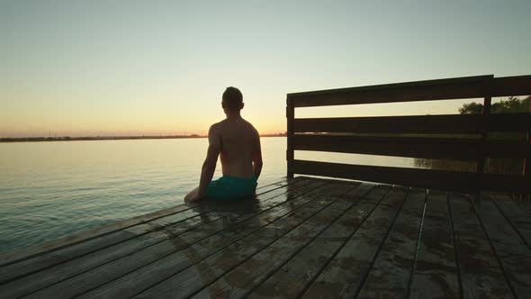 A Young Man is Sitting on the Edge of the Pier and Watching the Sunset