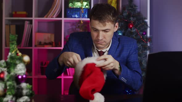 Suspicious Man in Santa Hat Looks Around Sitting in Office