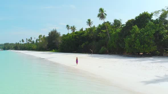 Aerial Slow motion: woman walking on white sand beach turquoise water tropical coastline
