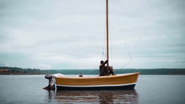 Master and His Assistant Work on Wooden Sailboat on Lake Installing Mast