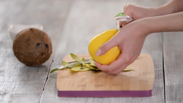 Hands Peeling Mango Over Cutting Board.