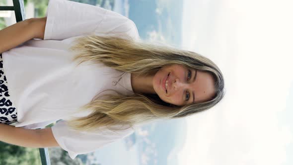 Blonde Woman Looks at the Camera Standing on the Background of Beautiful Mountains