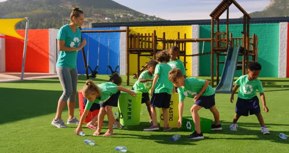 Side view of Caucasian female teacher teaching schoolkids about bottle recycle in the school playgro