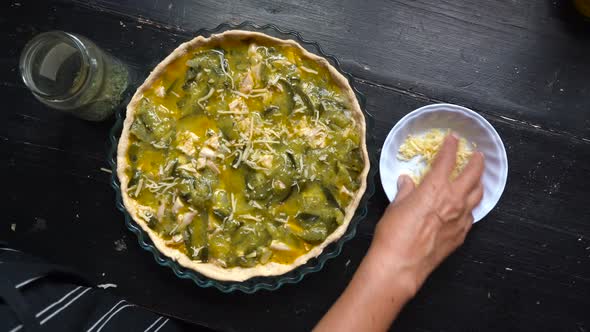 Woman's Hand Sprinkling Grated Cheese On Top Of Zucchini Pie Before Baking. overhead shot