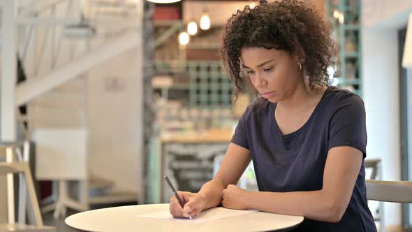 Thoughtful Young African Woman Doing Paperwork in Cafe 