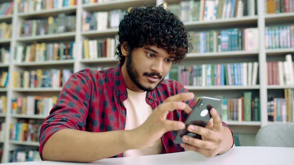 Happy Indian or Arabian Millennial Guy Freelancer or Student Using His Smartphone Chatting with
