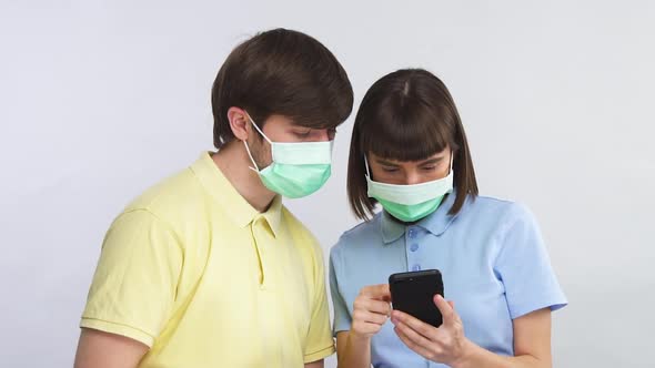 Young Couple in Protection Masks Scrolling Phone and Discussing News