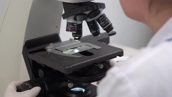 Biochemist analyzing sample through microscope glass, laboratory diagnostics. 