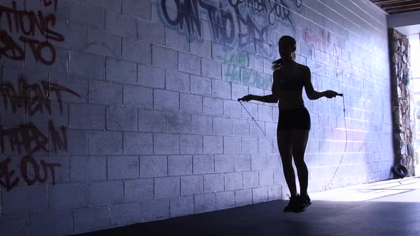 Silhouette of a young woman jump roping in a gym.