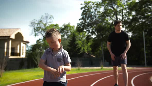 Father and His Little Son in Sportswear are Smiling Fooling Around and Making Faces During Training