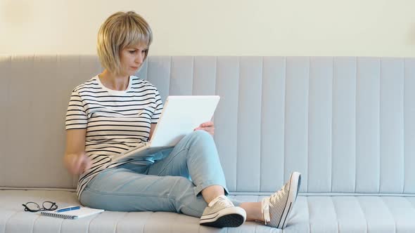 An Elderly Beautiful Woman Works at Home at a Laptop in the Home Office