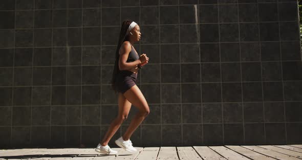 African american woman exercising outdoors wearing wireless earphones stretching in the city