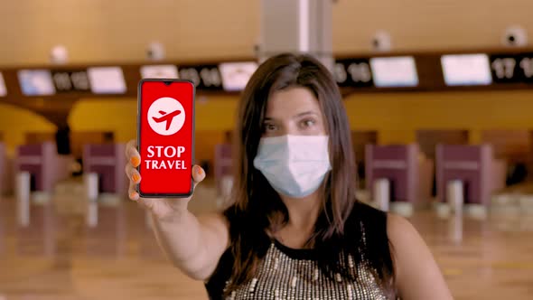 Woman, in Protective Mask, Holds Smartphone with COVID-19 Icon, Text - Stop Travel, on Screen