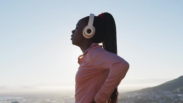 African american woman exercising outdoors putting on wireless headphone in countryside at sunset