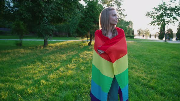 Smiling Woman Holding Rainbow Flag Around Body.