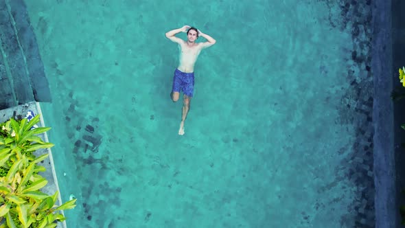 Man in Blue Trunks Lays on the Blue Water Pool