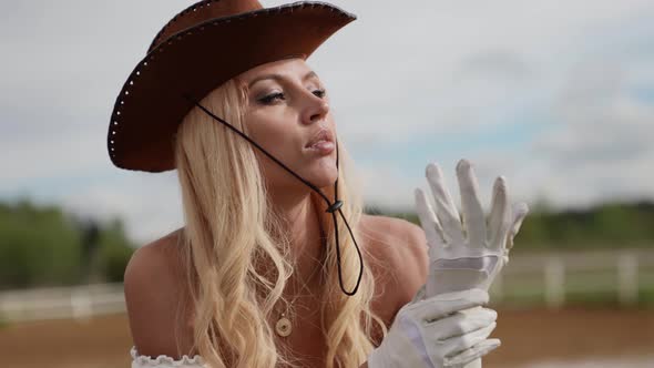 Sexy Blonde Lady with Traditional Leather Hat of Cowboy is Standing on Ranch