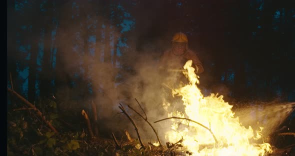 Fire Fighter with Safety Equipment and Axe Extinguishing Fire in Forest at Night