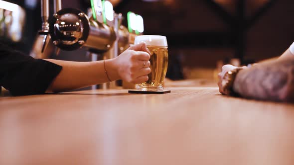 tattooed client picking up a pint of beer from wooden bar table