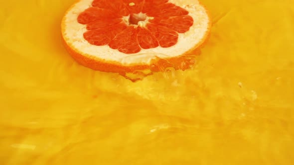 Grapefruit slices fall into the water on an orange background. Slow motion.