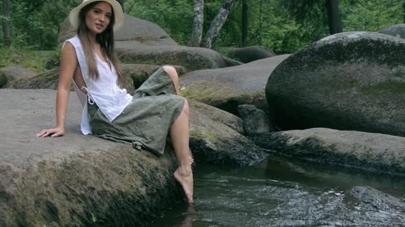 Beautiful girl sitting on stone in forest and splashing in water
