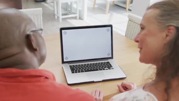 Happy senior diverse couple wearing shirts and using laptop with copy space in living room